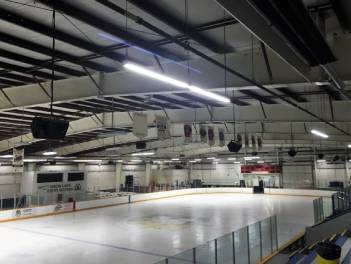 A indoor hockey rink with newly installed speakers hanging from the roof.